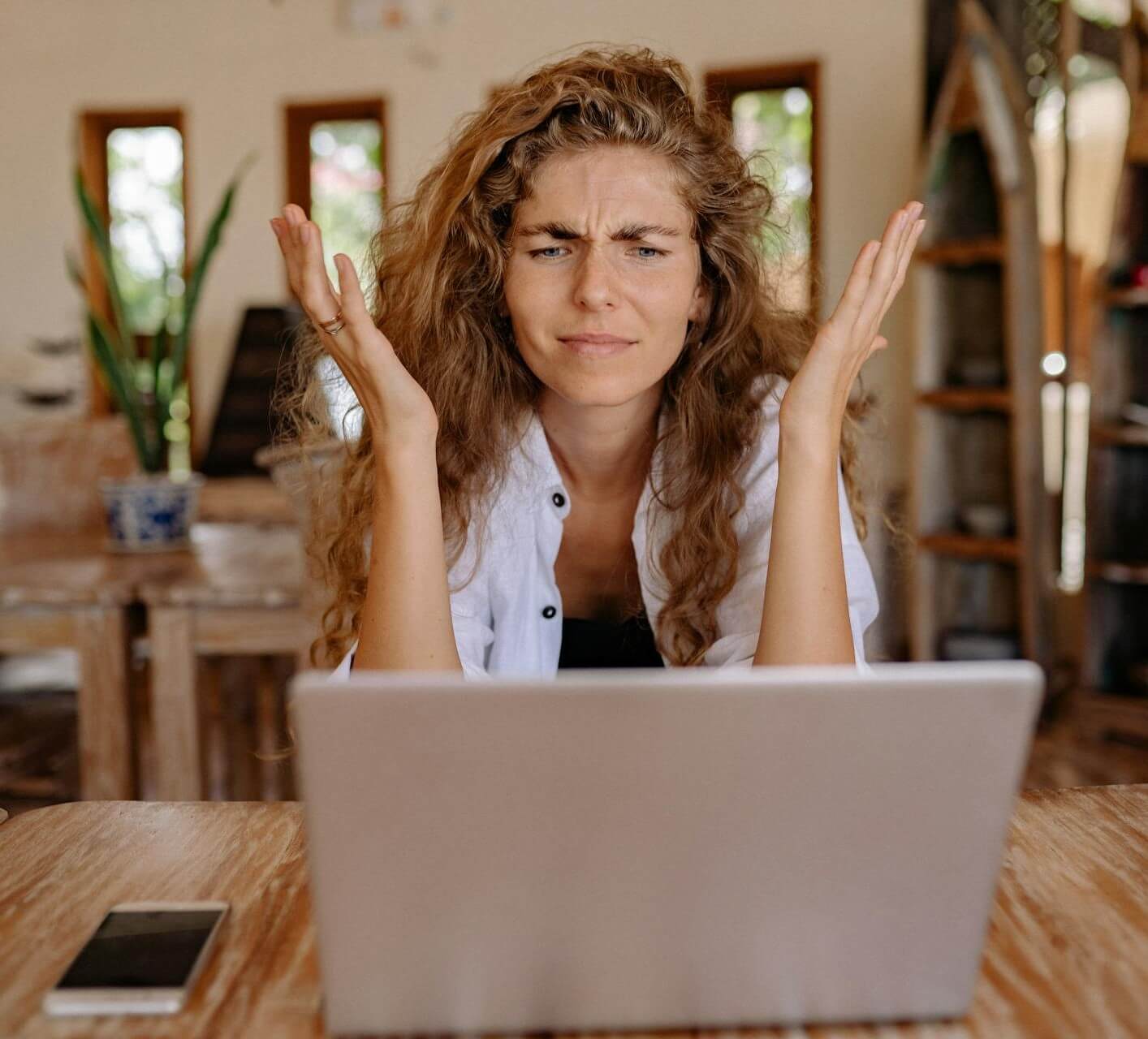 A person looking stressed while working on a laptop with a cup of coffee and some papers on the table.